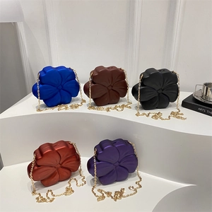 Five 3D flower acrylic evening bags in bold colors with gold chain straps on white steps