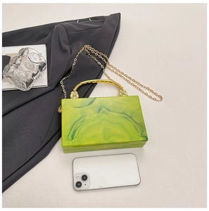 Detail view of green marble acrylic clutch bag with gold handle and chain on fabric
