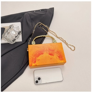Detail of orange marble acrylic clutch bag with gold curved handle and chain strap