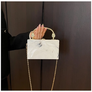 Detailed view of white marble acrylic clutch bag with gold handle and chain strap