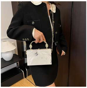Detail of marble acrylic clutch bag with gold chain strap and spherical top handle