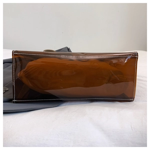 Detailansicht des rechteckigen Bodens und der weißen Doppelnaht an der bernsteinfarbenen PVC-Tasche