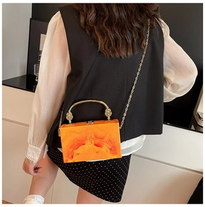 Detail of orange marble acrylic evening bag with gold handle and chain on model