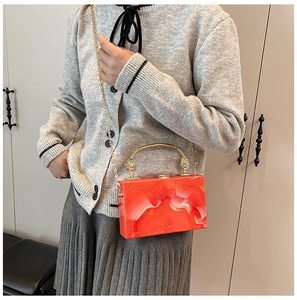Detail of orange acrylic box bag with white fluid texture and golden metal handle