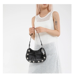 Détail du sac hobo noir brillant avec grands clous argentés sur une robe en maille