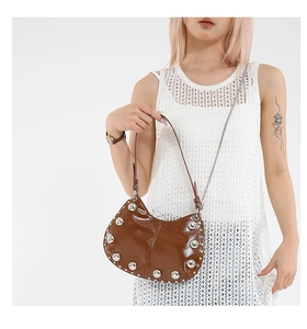 Detail of brown leather half-moon bag featuring large silver studs and metallic chain strap