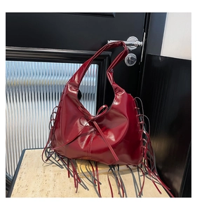 Vue détaillée du sac à bandoulière en cuir verni rouge foncé avec franges et nœud