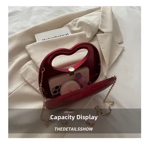 Detail showing red heart-shaped clutch interior with phone, cosmetics and gold chain