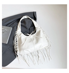Détail d'un sac hobo en cuir blanc avec franges et nœud posé sur un costume gris