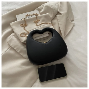 Detail of black heart-shaped handbag with matte finish and gold chain strap on fabric
