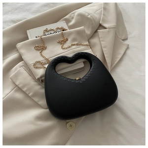 Detail view of heart-shaped black handbag featuring gold chain and textured cut-out handle