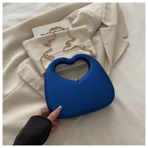 Detail of matte navy heart clutch bag with circular groove handle and gold chain strap