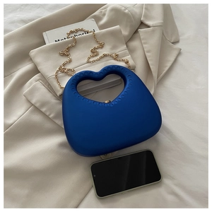 Detail of blue heart-shaped tote with gold chain strap on beige fabric backdrop