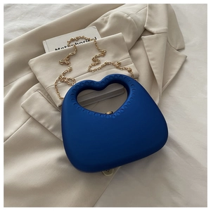 Detailed shot of dark blue heart-shaped acrylic bag with gold chain strap on blazer