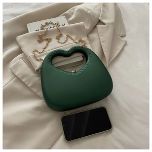 Detail of dark green heart-shaped bag with matte texture and gold metal chain strap