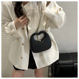 Detail of black heart-shaped handbag with golden twist-lock and slim metal chain strap