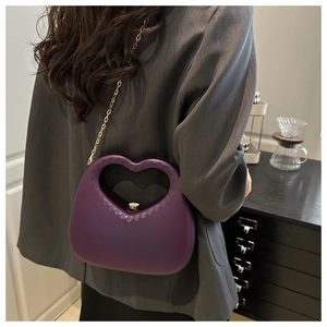 Detail of a purple heart-shaped acrylic bag with a gold chain strap on a model's shoulder