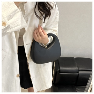 Detail of crescent shoulder bag with round handle and gold chain on white coat