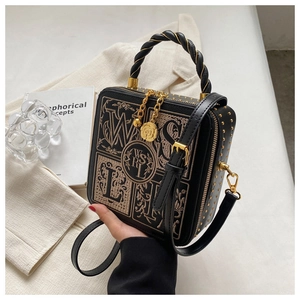 Close-up of vintage embroidery and gold studs on a black square crossbody handbag