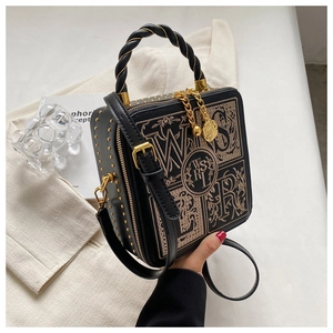 Detail of black box bag featuring gold embroidery shield and metallic studs