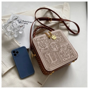 Detail of embroidered small square box bag with braided handle and gold rivets
