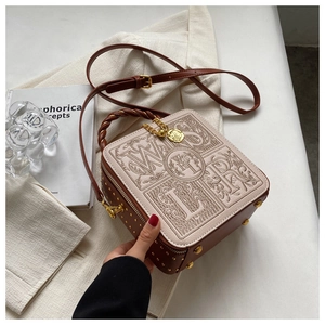 Detail of vintage box bag with embossed retro letters and rose gold charm on blazer