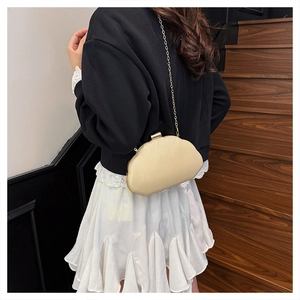 Detail of a beige shell-shaped evening bag with a fine gold chain worn by a model