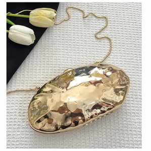 Detail of golden metal clutch bag featuring wave texture and fine snake chain strap