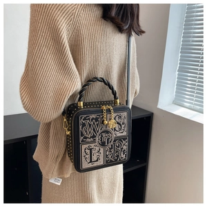 Detail of a vintage black box bag with gold embroidery and braided handle on model