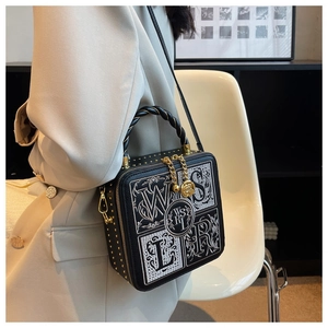 Close-up of black box bag with white letter embroidery, gold rivets, and camellia charm