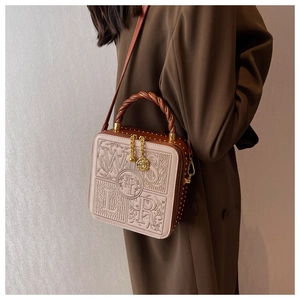 Detail of embroidered square box bag featuring WSLR embossing and woven handle on model