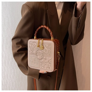 Detail of embroidered box bag with embossed letters, woven handle, and metal floral pendant