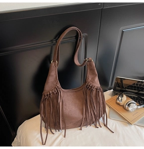 Close-up of deep brown suede shoulder bag featuring layered fringe and gold hardware