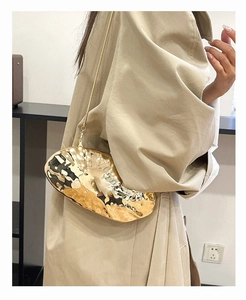 Detailed shot of golden shell-shaped evening bag with liquid metal texture and chain strap