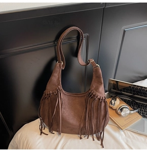 Detail of a brown suede hobo bag with long tassels and golden metal buckle hardware