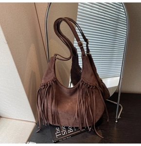 Detail of brown suede hobo bag with long fringes and gold buckle on wooden surface