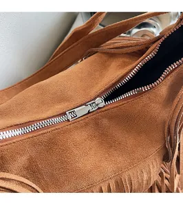 Close-up of silver metal zipper and brown suede texture on vintage tassel bag