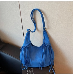 Detail of electric blue suede hobo bag featuring long tassels and wide shoulder strap