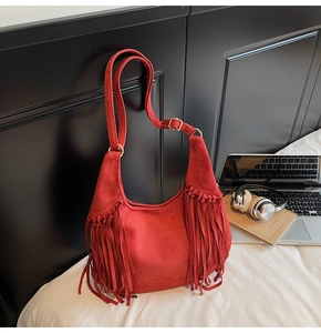 Macro view of red suede hobo bag with fringe details and gold hardware in home setting