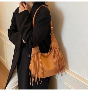 Detail of brown suede hobo bag featuring long tassels and gold adjustable buckle strap