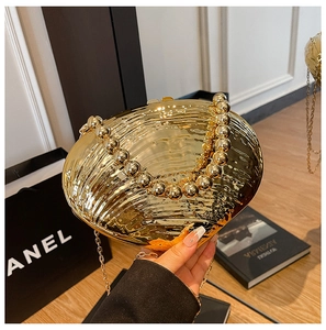 Détail d'une pochette dorée en forme de coquillage avec poignée perlée et chaîne en métal