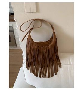 Detail of a brown suede hobo bag with long fringes and vintage hardware on a sofa