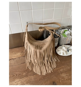 Close-up of a khaki suede hobo bag with tiered tassels on a wooden surface