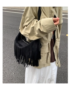 Detail of black suede shoulder bag featuring long tassels and metallic zipper closure