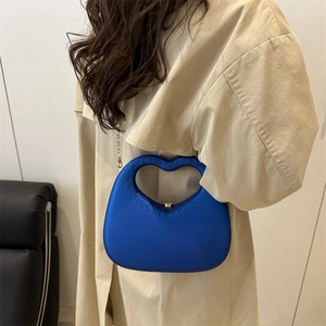 Klein blue heart-shaped handbag with matte finish and gold chain strap on model