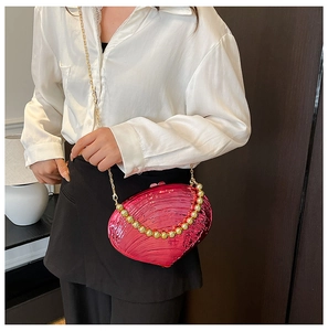 Close-up of fuchsia shell-shaped acrylic clutch bag with gold chain and beaded handle