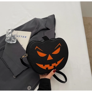 Détail d'un sac bandoulière citrouille d'Halloween noir à côté de livres et un verre