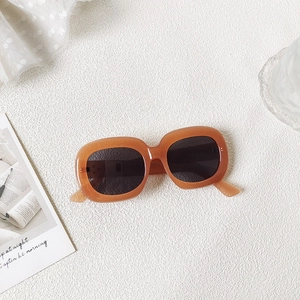 Detail view of oval sunglasses with thick orange frames and dark lenses on white lace