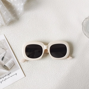 Detail of retro oval sunglasses with cream white frame and dark lenses on a sandy background