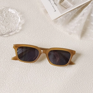 Détail de lunettes de soleil rectangulaires ambre sur une surface décorative blanche texturée